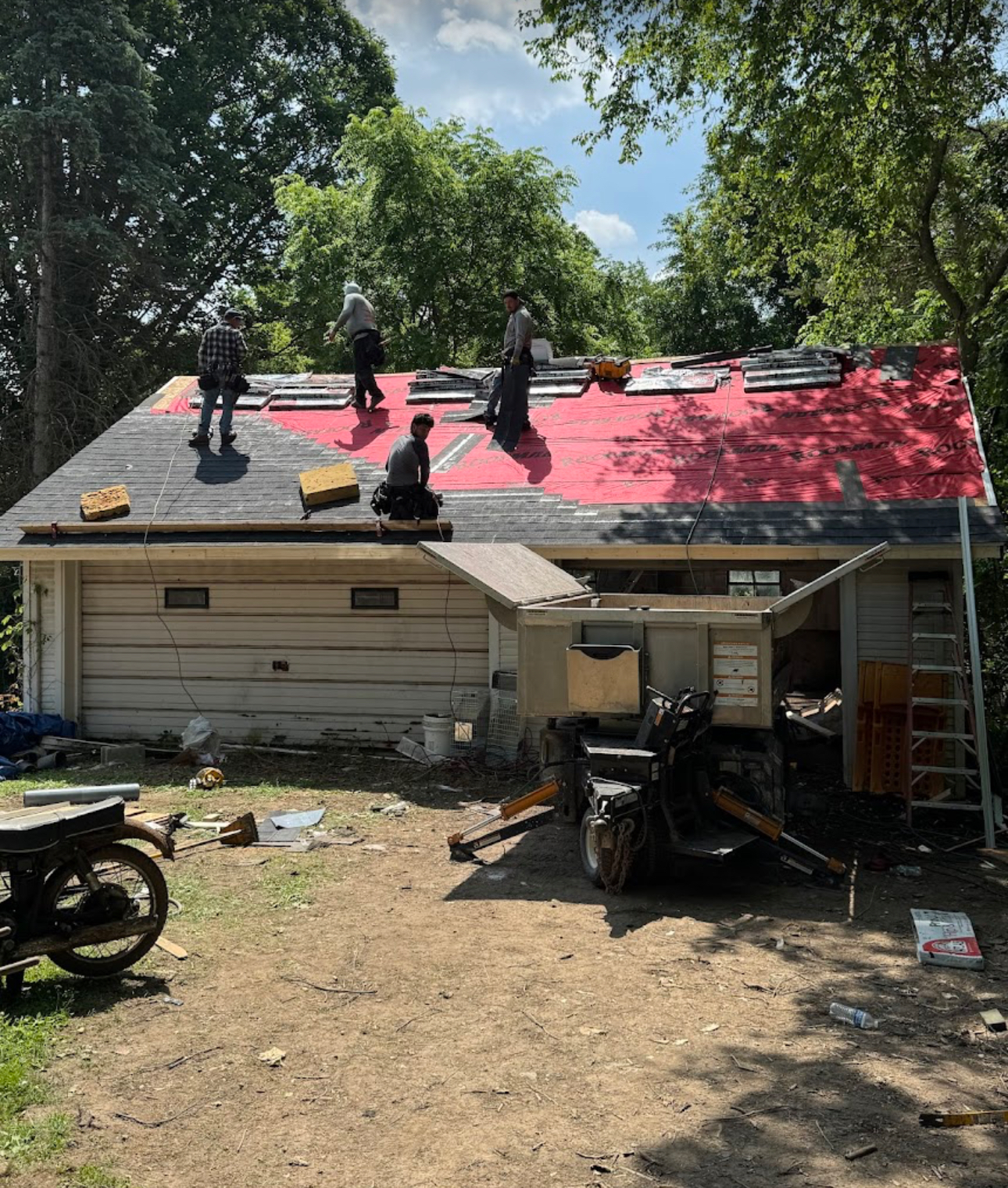 Crew installing underlayment and new shingles on a detached garage roof with a dump trailer on site. Roofing work by Alba Pro Construction serving Hackensack, NJ.