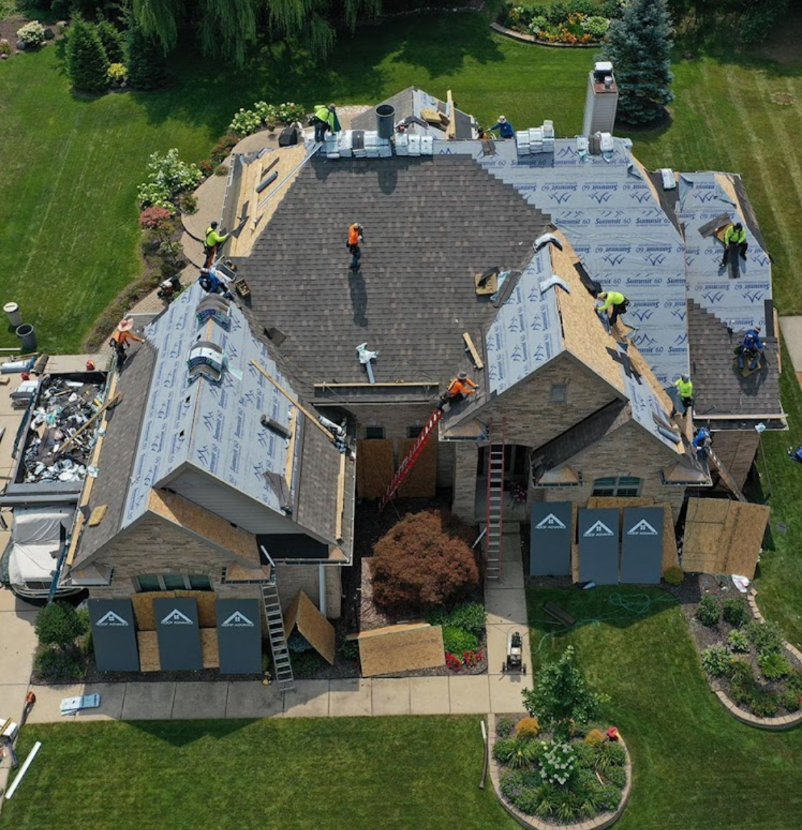 Overhead view of a roof replacement in progress with underlayment on several slopes and a debris trailer at the driveway. Roofing work by Alba Pro Construction serving New Jersey, NJ.