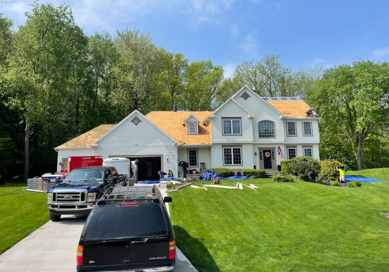 Roof replacement in progress on a large white home with the old shingles removed and roof decking exposed. Roofing work by Alba Pro Construction serving Hackensack, NJ.
