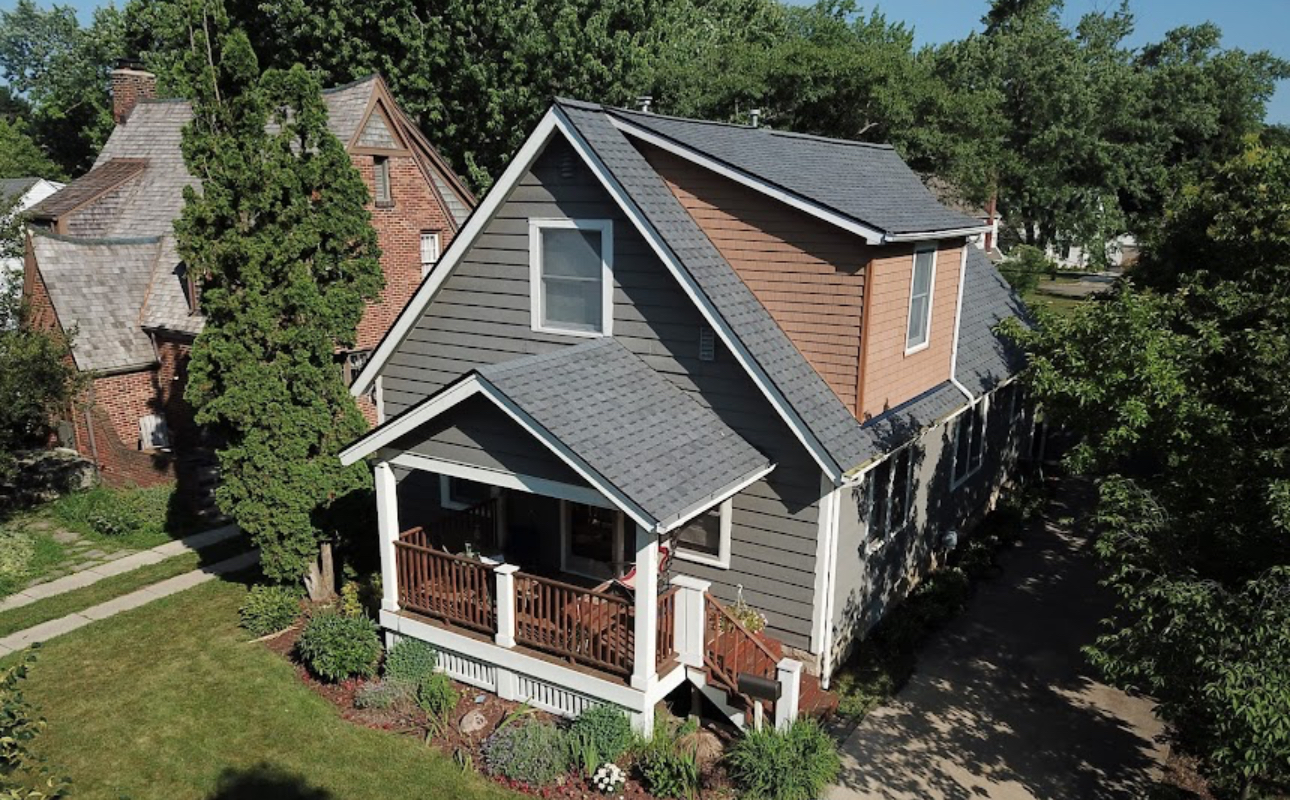 Aerial view of a completed charcoal shingle roof with new gutters on a grey cape style home. Roofing work by Alba Pro Construction serving Midland Park, NJ.