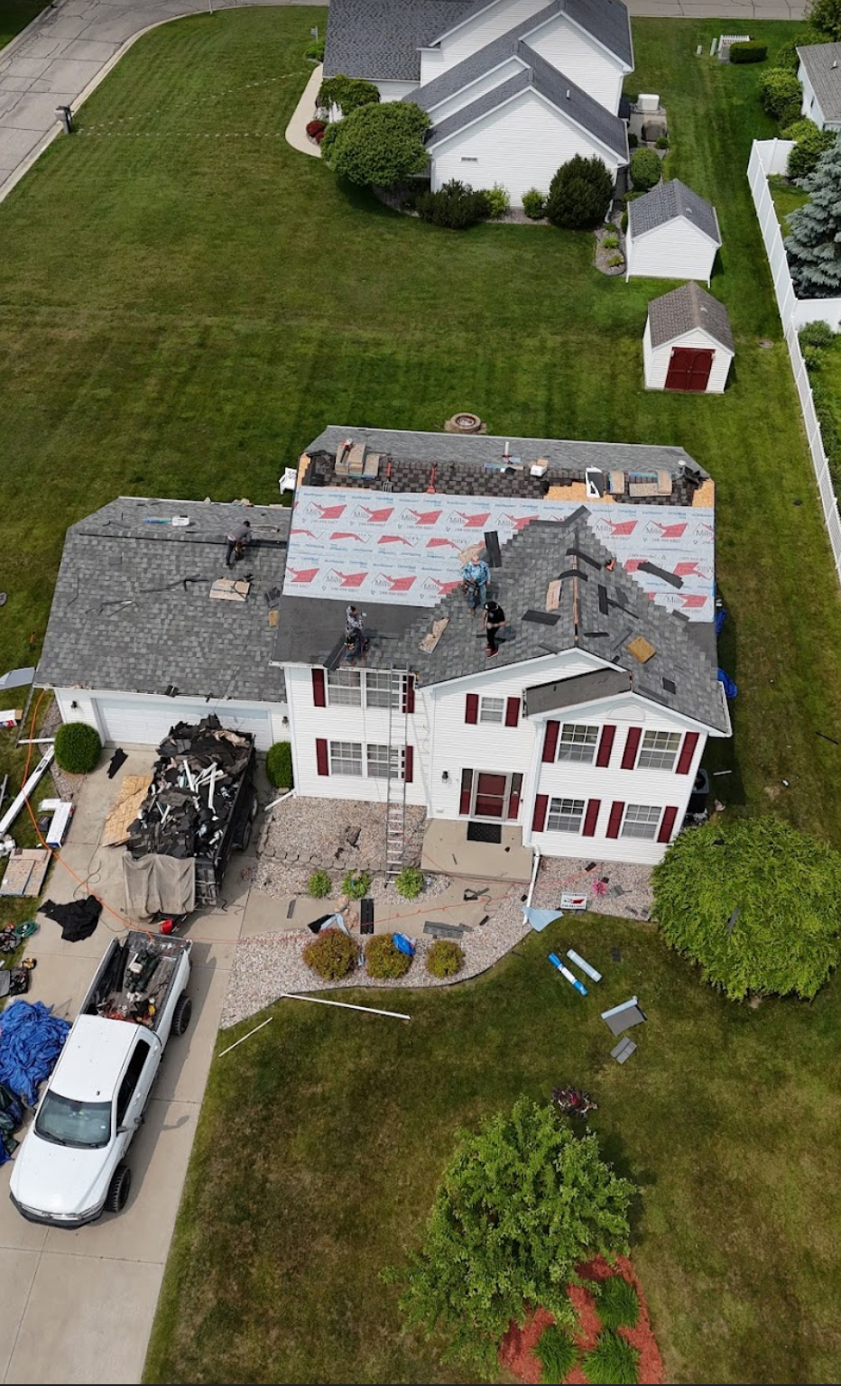 Aerial view of a roofing crew installing shingles and synthetic underlayment on a two-story home with debris contained beside the driveway. Roofing work by Alba Pro Construction serving Paramus, NJ.