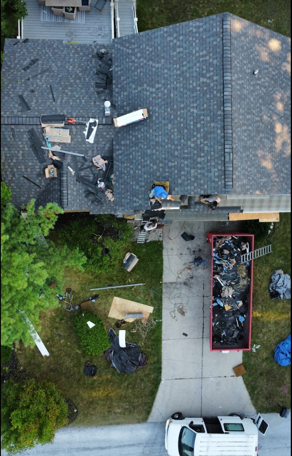 Overhead view of roofers completing a grey architectural shingle roof with a debris container positioned in the driveway. Roofing work by Alba Pro Construction serving Englewood, NJ.