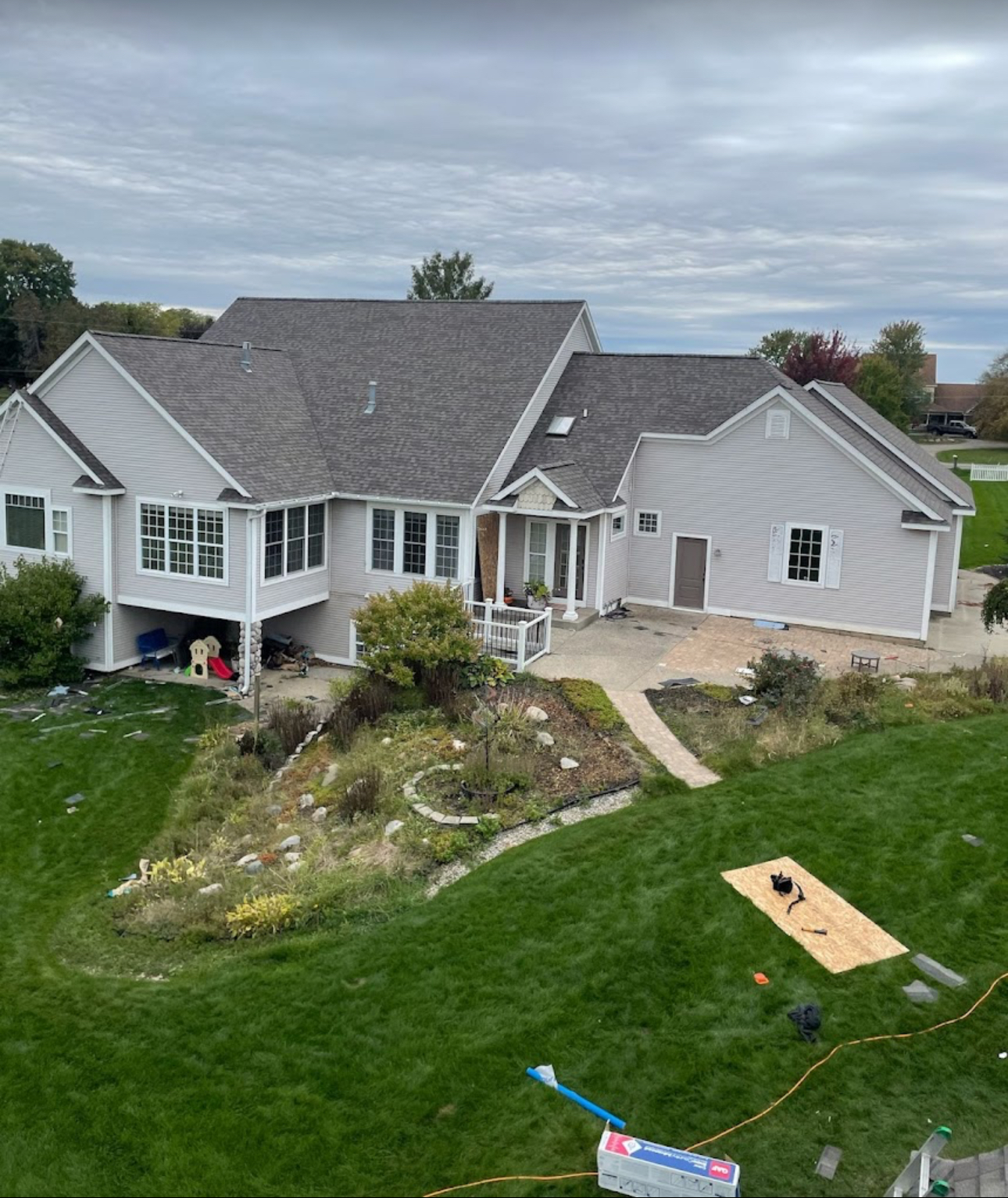 Rear view of a large home during a roof replacement with old shingle debris on the lawn and plywood staged for the crew. Roofing work by Alba Pro Construction serving Wood-Ridge, NJ.