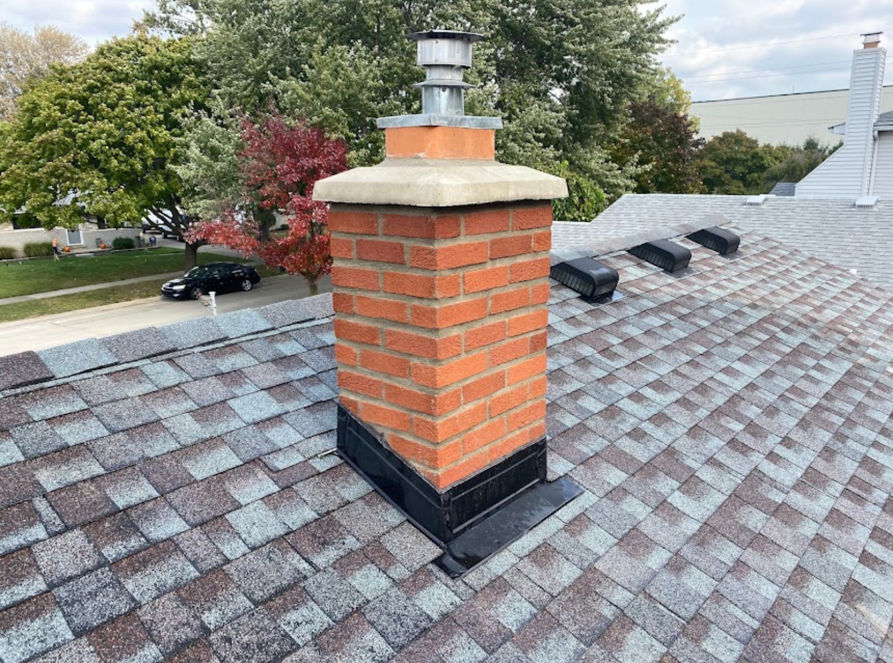 Brick chimney with a new concrete crown and black flashing integrated into a completed architectural shingle roof. Roofing work by Alba Pro Construction serving Little Falls, NJ.