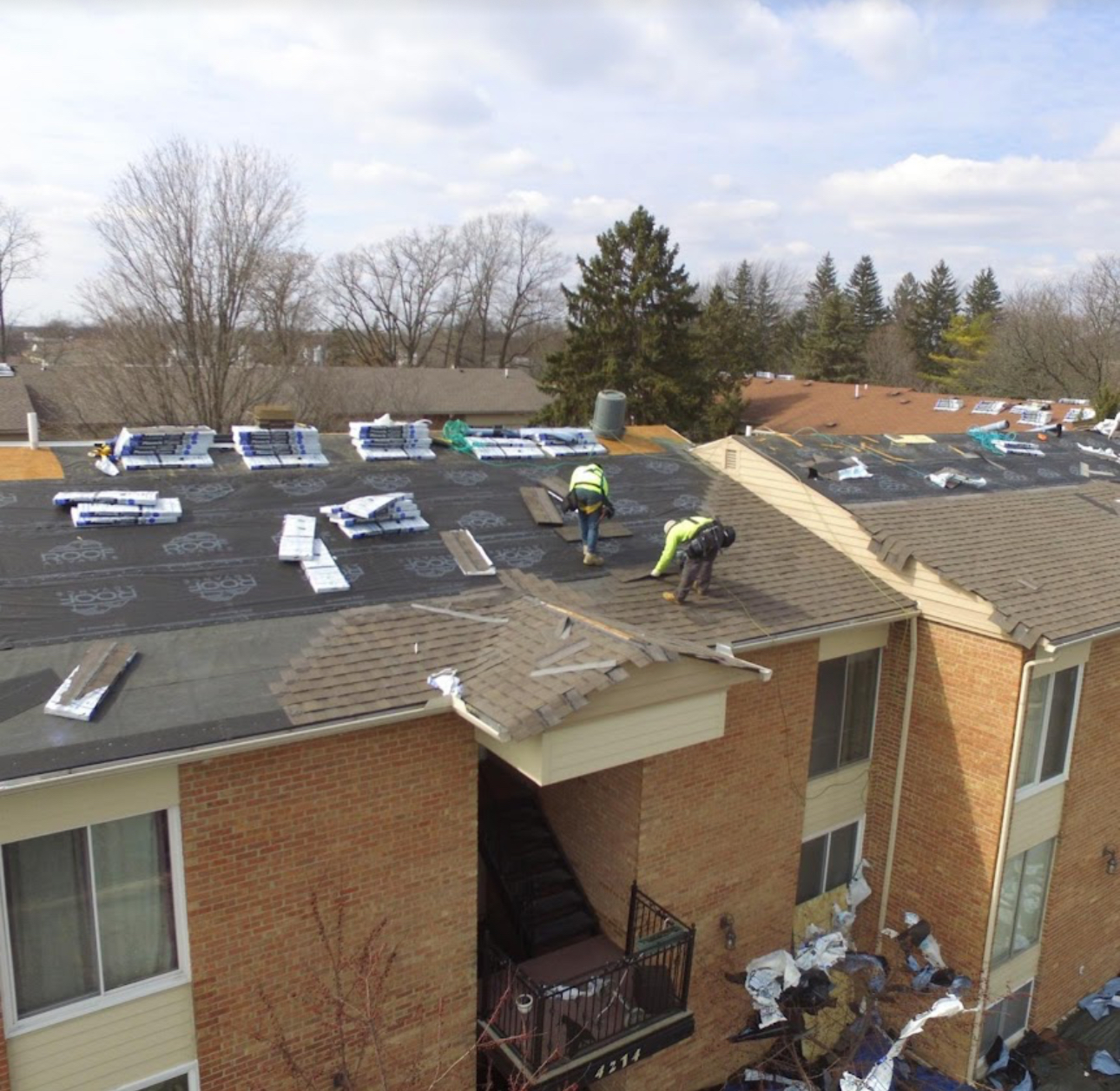 Roofers stripping shingles from a multi-family brick building with underlayment and shingle bundles staged across the roof. Roofing work by Alba Pro Construction serving Paterson, NJ.