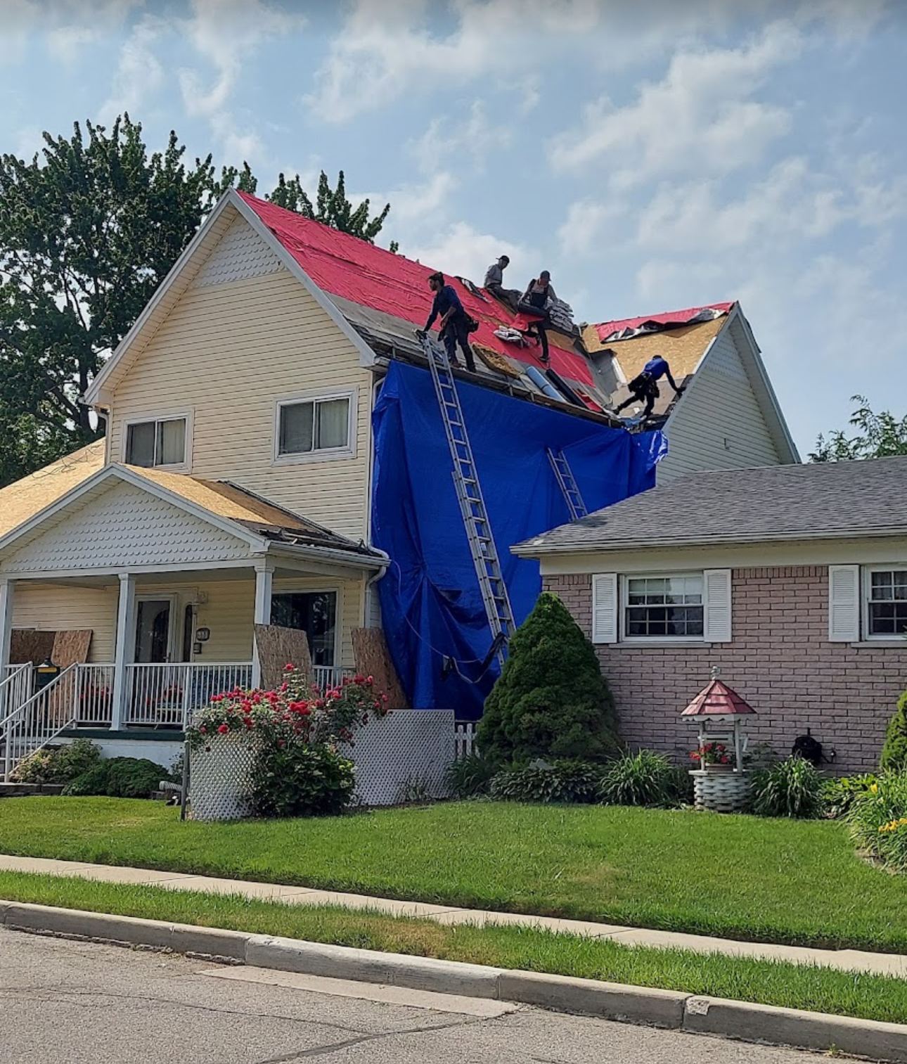 Roofing crew working on a yellow two-story home with red underlayment installed and a large tarp shielding the siding. Roofing work by Alba Pro Construction serving Waldwick, NJ.