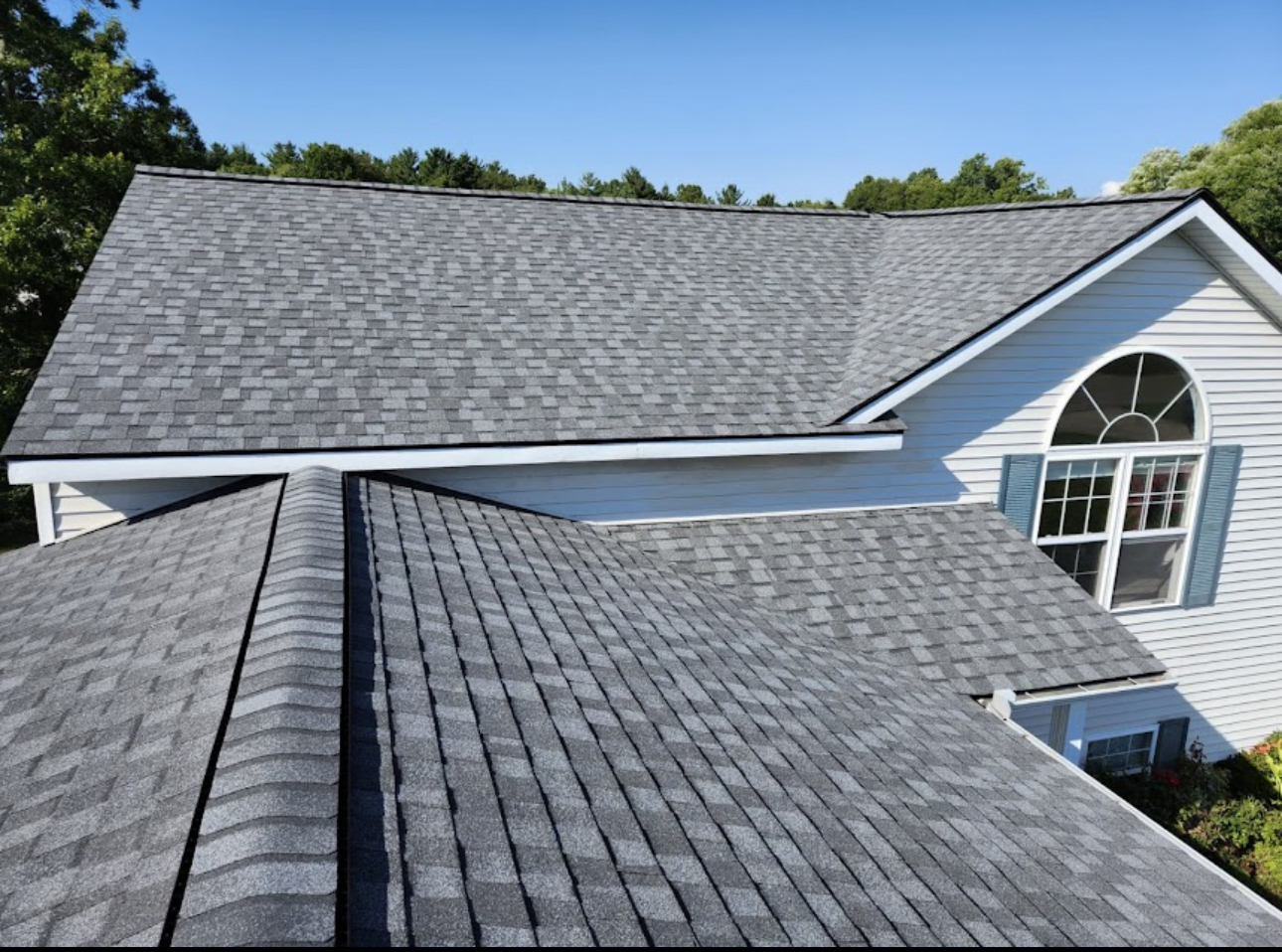 Close view of a completed grey architectural asphalt shingle roof on a home with white trim and an arched window. Roofing work by Alba Pro Construction serving River Edge, NJ.