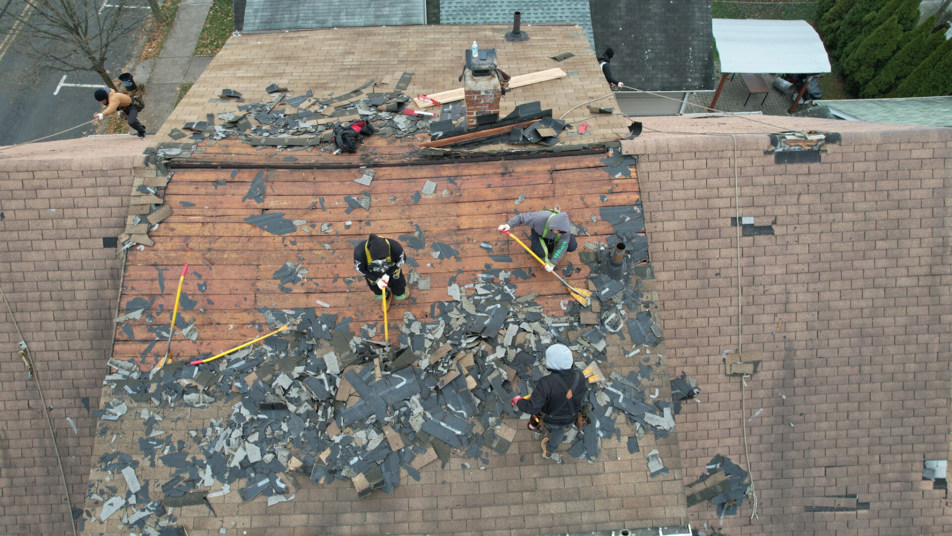 Roofers carefully removing multiple layers of old asphalt shingles. Roofing work by Alba Pro Construction serving Ramsey, NJ.